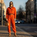 Módní modelka v oranžovém outfitu na městské ulici při zlaté hodině s rozostřeným pozadím.