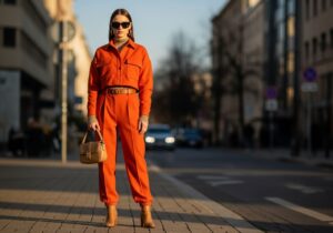 Módní modelka v oranžovém outfitu na městské ulici při zlaté hodině s rozostřeným pozadím.